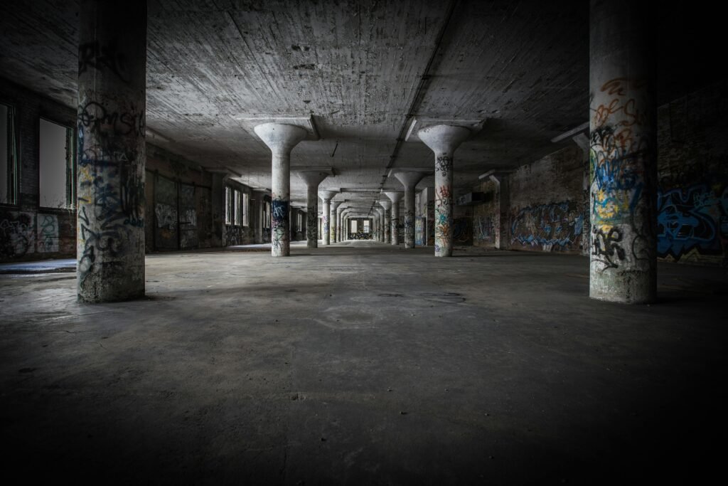 Moody interior of an abandoned warehouse featuring graffiti-covered columns and empty space.